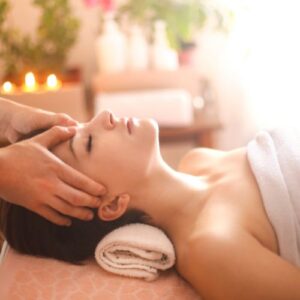 Massage visage apaisant sur lit spa. Serviette enveloppante, tête reposée. Éclairage doux, bougies et plantes. Atmosphère zen.